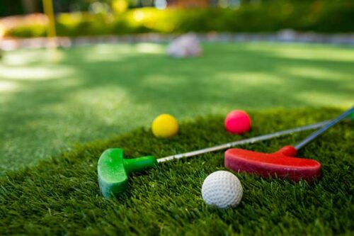 A pair of putt-putt golf clubs with a few balls on a grassy hill, as an example of one event idea to hold for young professional members in an association.