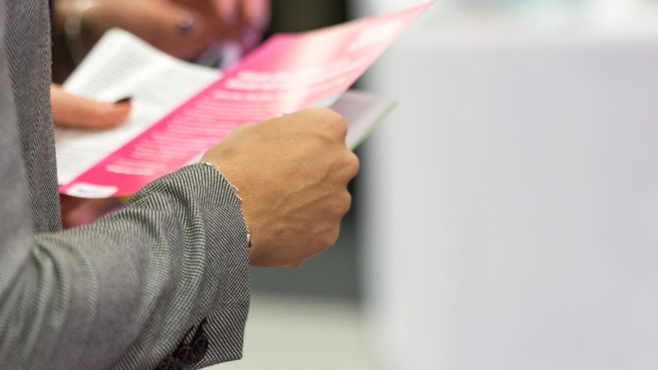 A close-up of a marketing flyer in a person's hands, spreading information about an association.