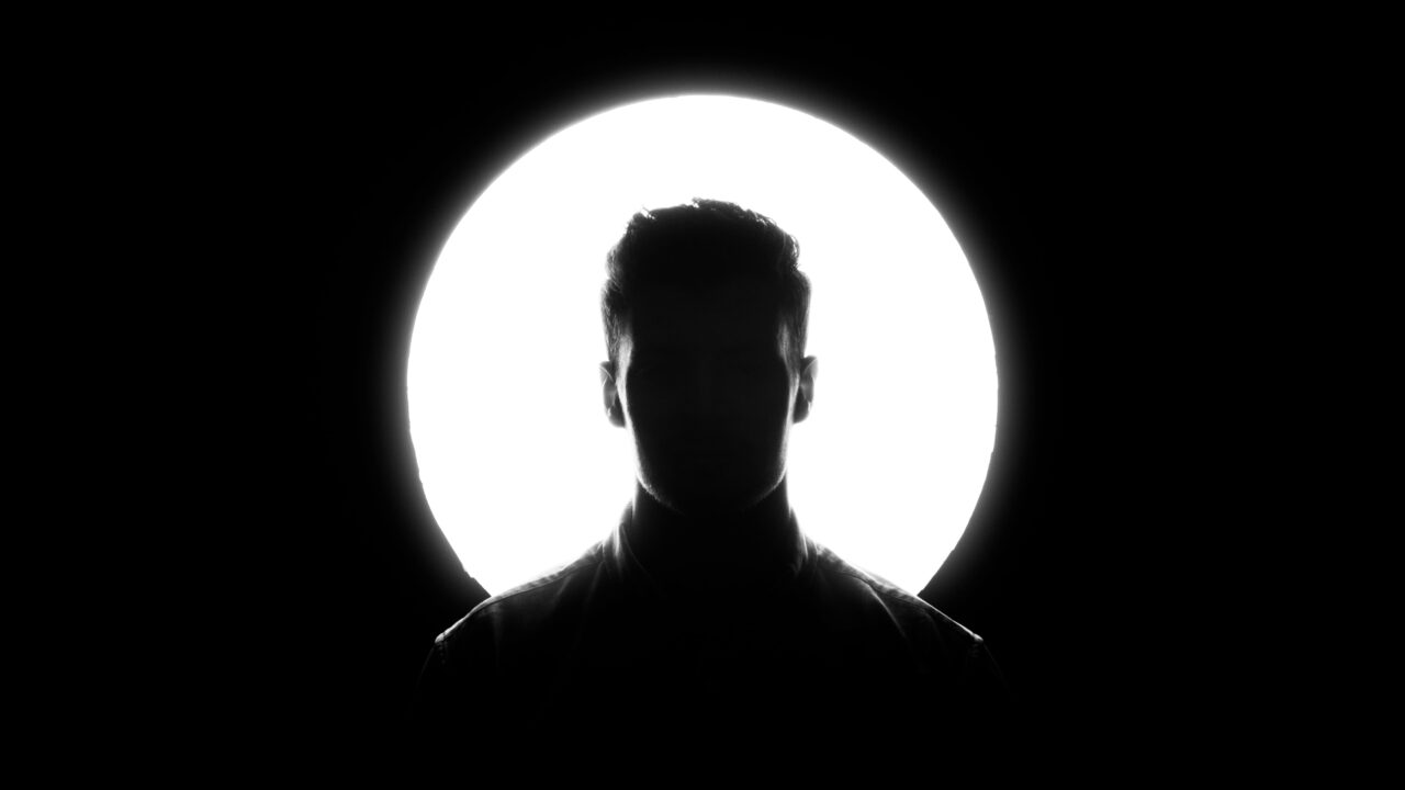 A bright spotlight backlighting a member's silhouette against a black background.