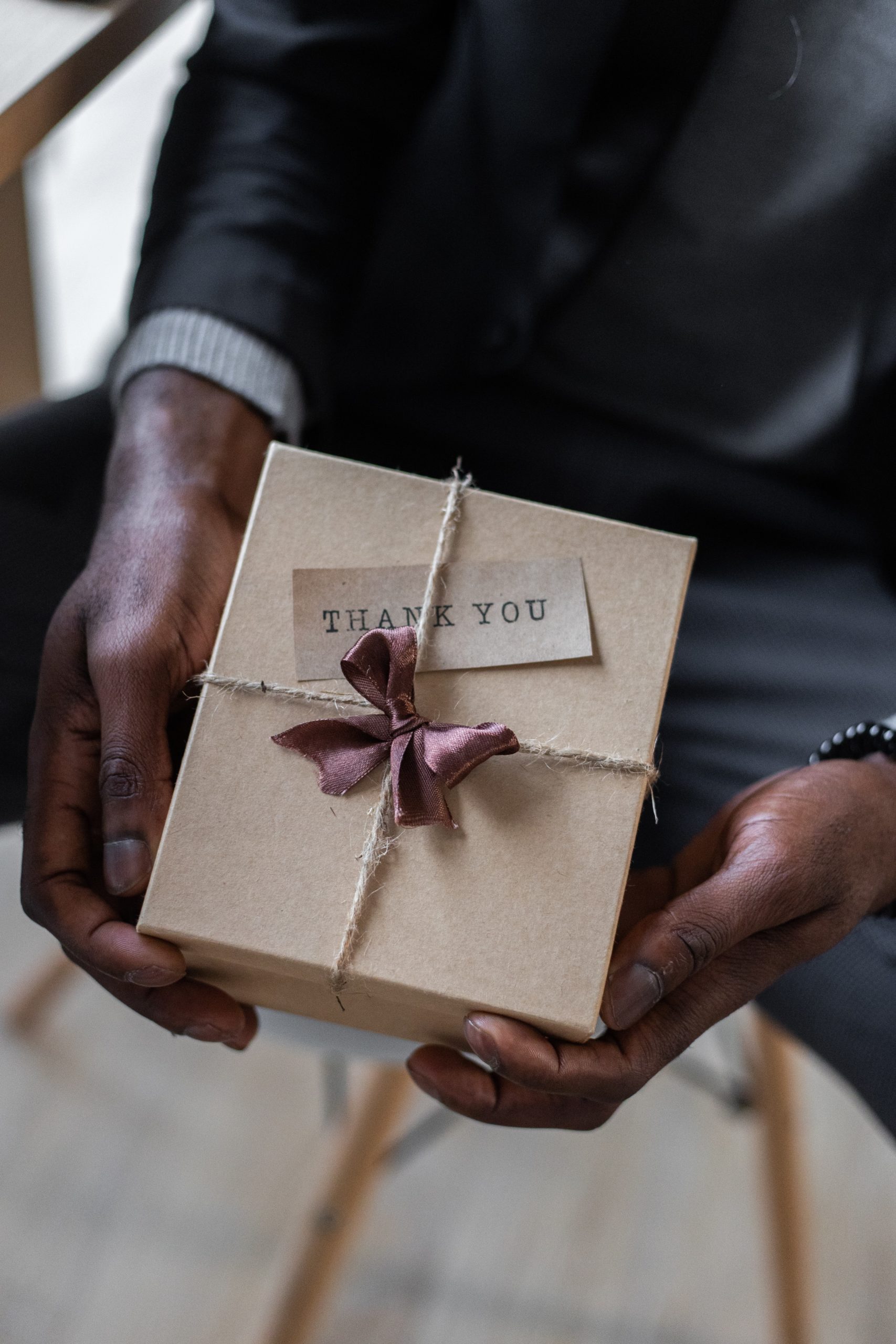 A person offering a hand-wrapped gift box with a thank you note to show member appreciation.