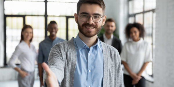 Close up headshot portrait of happy businessman shaking hand posture. Different smiling ethnicity businesspeople standing behind of male company chief. Leader of multi-ethnic team concept.